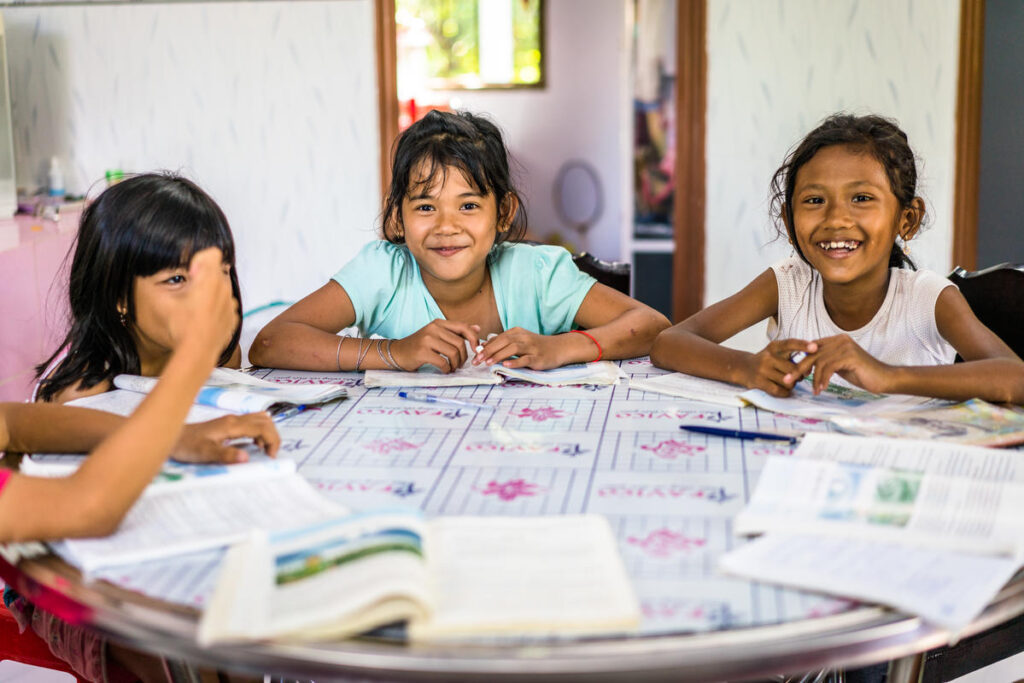 A table with 3 young children smiling and holding workbooks.